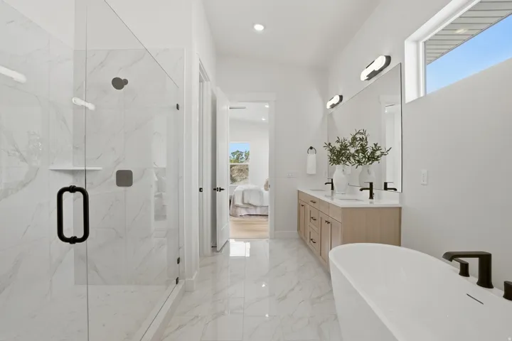 Spacious bathroom featuring a glass-enclosed shower with white marble-finish tiling, a freestanding soaking tub, a dual vanity with light wood-finish cabinetry, and a clerestory window