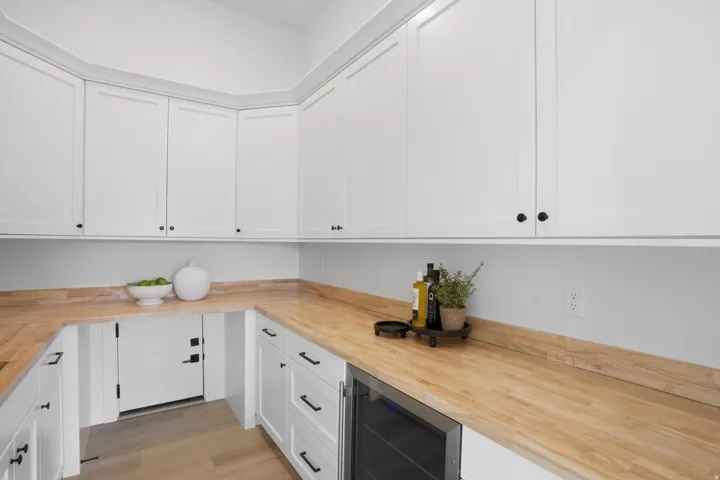Built-in wine refrigerator, wood-finish countertops, white shaker cabinetry, black hardware, and light wood-finish flooring