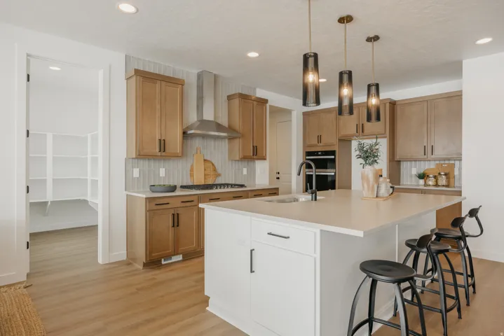 Spacious kitchen featuring an expansive center island, pendant lighting, stainless steel appliances, a tile backsplash, and wood-finish flooring