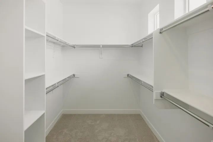 Walk-in closet with integrated shelving, multiple hanging rods, and carpet flooring