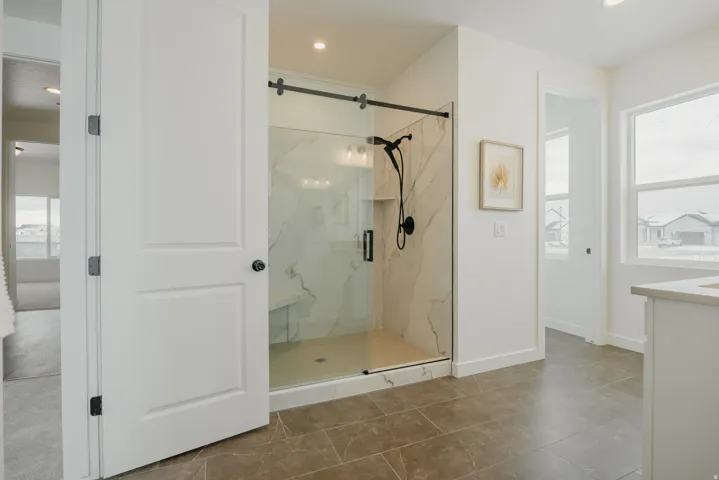 Spacious shower enclosure with a clear glass door, black hardware, and an integrated bench, complemented by large format floor tiling