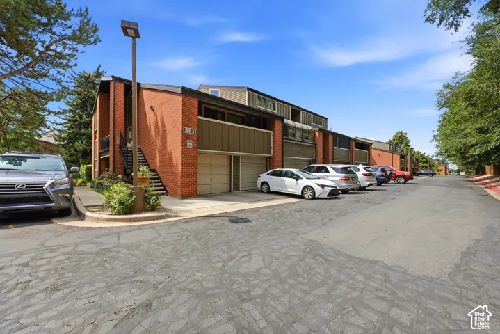Modern industrial warehouse featuring brick and metal panel exterior with multiple garage-style bay doors, ample paved parking area, and mature landscaping