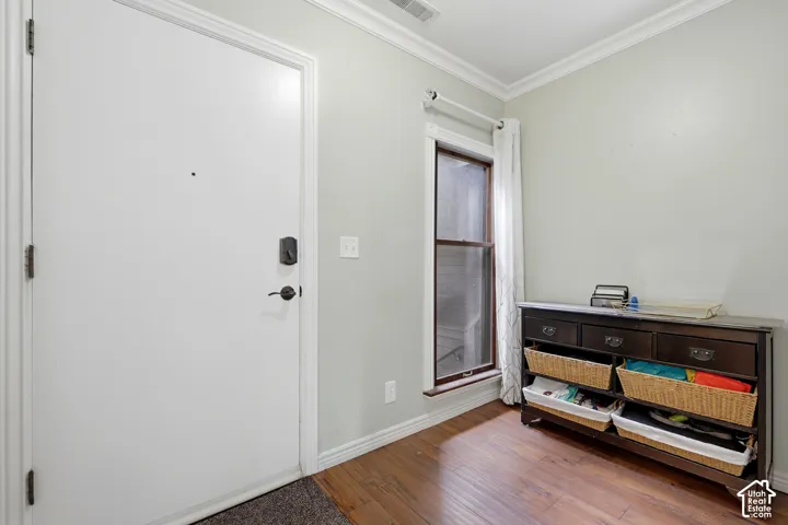 Hardwood-finish flooring, crown molding, white trim, and a window with a wood-finish frame