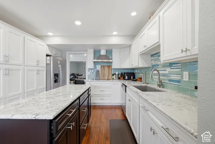 Kitchen featuring white shaker cabinetry, stainless steel appliances, a center island with contrasting cabinetry, light-toned countertops, and a tiled backsplash