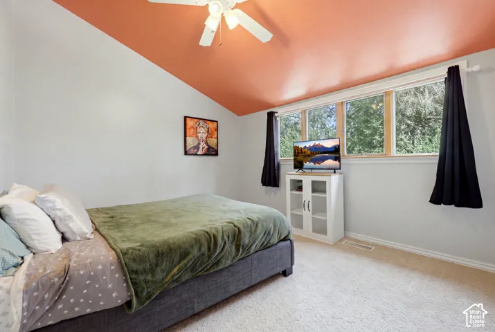Vaulted ceiling with an overhead fan, light-toned carpeting, and a multi-pane window with wood-finish framing