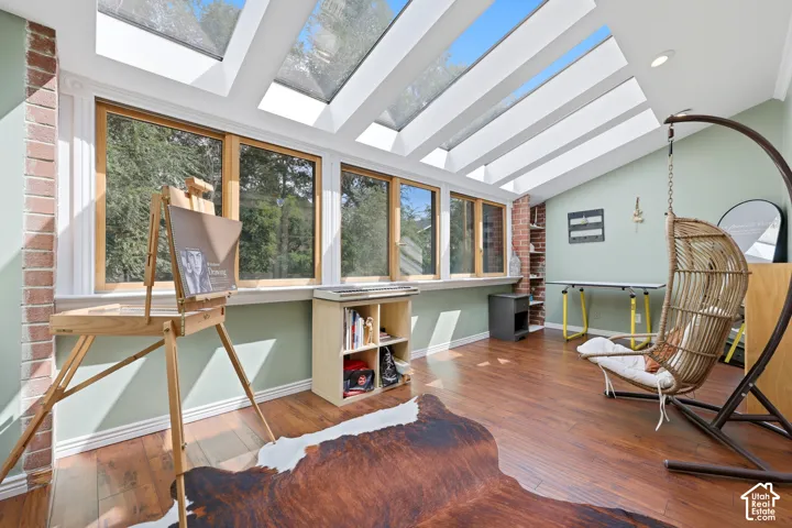 Room featuring expansive skylights, a wall of windows, exposed brick accents, and wood-finish flooring
