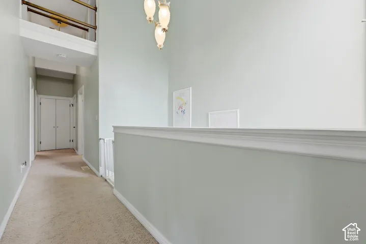 Vaulted ceiling with an attached pendant light fixture, white wall paneling, and a carpeted hallway