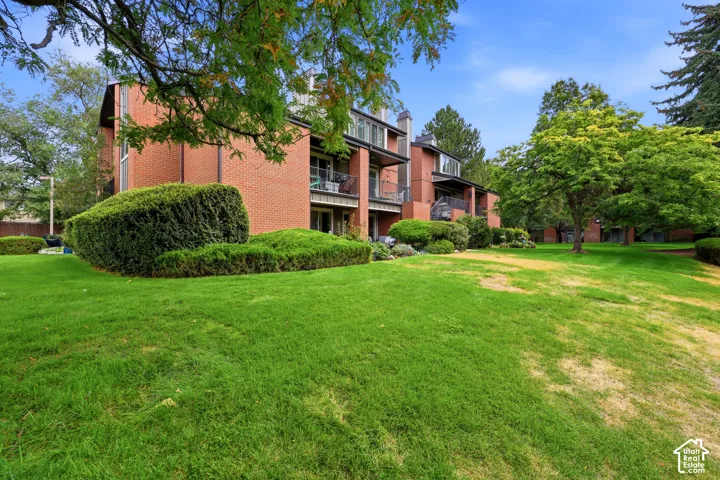 Brick exterior construction, multiple private balconies, expansive green lawn, mature trees, and sculpted shrubbery