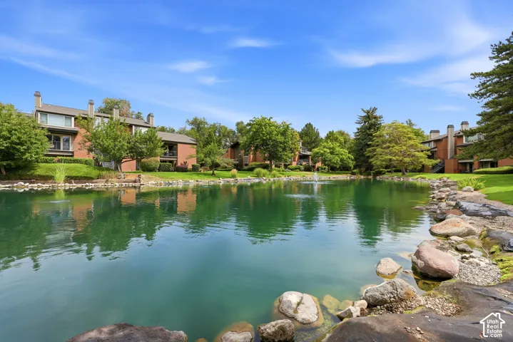 Waterfront property featuring mature landscaping, lush green lawns, and a serene pond with natural stone edging