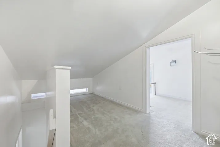 Carpeted loft space featuring sloped ceilings, white wall finishes, and recessed windows