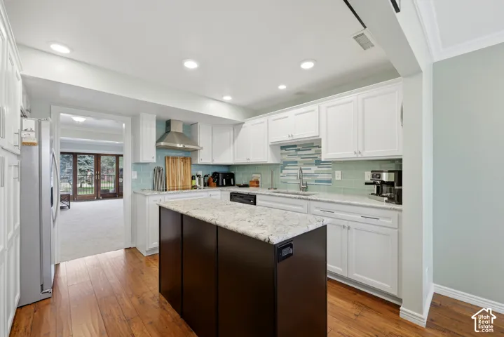 Kitchen featuring wood-finish flooring, white cabinetry, a dark-toned island with a light-toned countertop, a tile backsplash, and recessed lighting