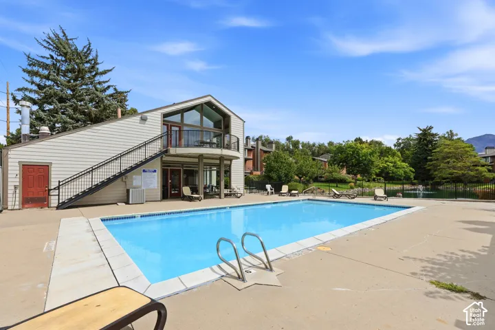 Outdoor swimming pool with concrete decking, featuring a multi-level building with an exterior staircase and a second-story balcony