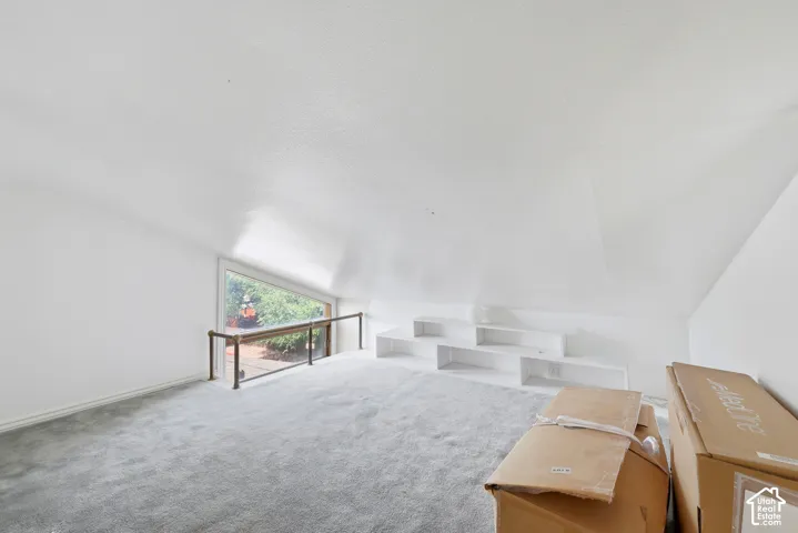 Attic space with sloped ceilings, light gray carpeting, built-in white shelving, and a large triangular window with a wood railing