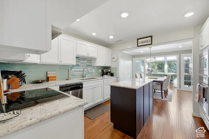 White cabinetry, light-toned granite countertops, wood-finish flooring, a kitchen island, and a decorative tile backsplash