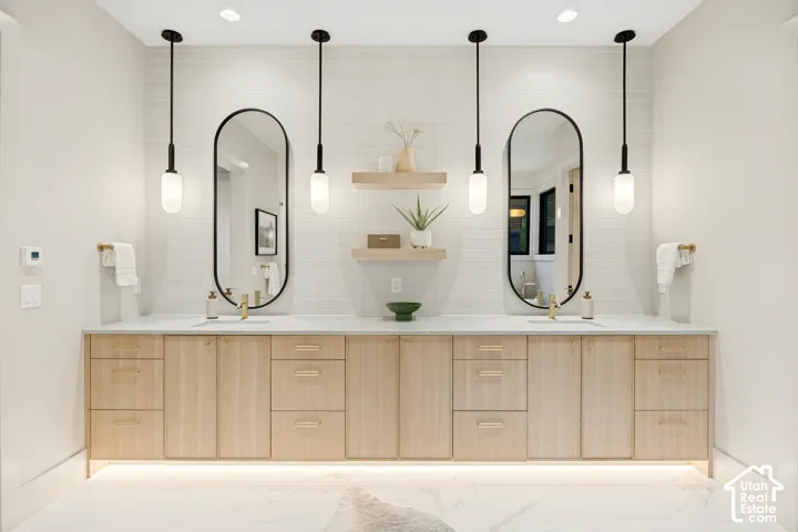 Dual oval mirrors with black frames, a light wood-finish vanity, dual pendant lights, and a white countertop