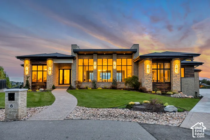 Modern architectural exterior featuring extensive stone detailing, large full-height windows, a paver walkway, and integrated exterior lighting