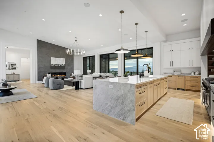 Expansive open-concept living space featuring wood-finish flooring, a contemporary kitchen island with a waterfall countertop, a modern linear fireplace with a textured accent wall, black-framed windows, and recessed lighting