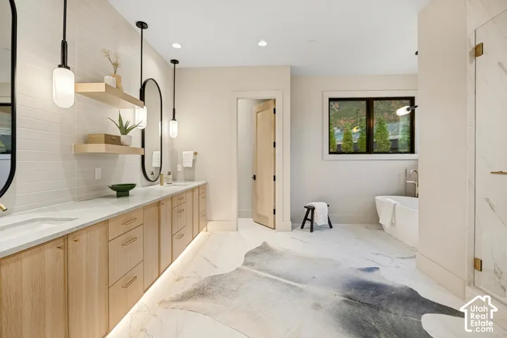 Double vanity with light wood-finish cabinetry and undermount sinks, illuminated by pendant lighting and under-cabinet strip lighting