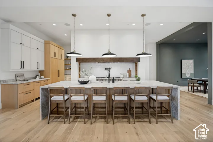 Spacious kitchen featuring a large island with countertop seating, light wood-finish flooring, recessed lighting, and mixed-material cabinetry