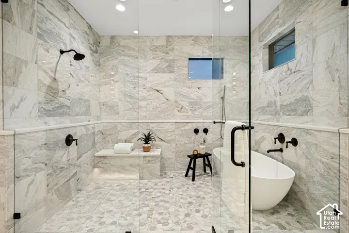 Spacious walk-in shower with stone tile walls, pebble-finish flooring, built-in bench, and freestanding soaking tub