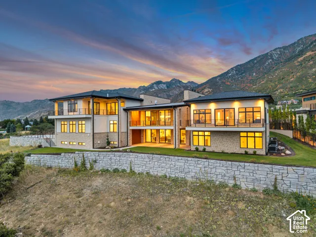 Modern multi-level exterior with extensive glazing, stone veneer accents, multiple balconies with glass railings, and a tiered retaining wall system