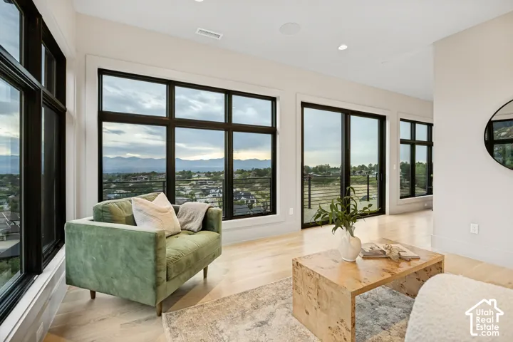 Expansive window array, light wood-finish flooring, recessed lighting, and a sliding glass door providing outdoor access