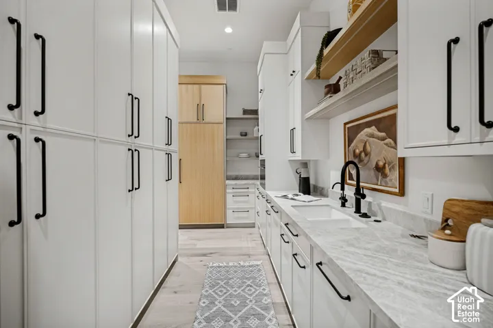 Extensive white cabinetry with black hardware, light wood-finish flooring, undermount sink with a matte black faucet, and light-toned countertop