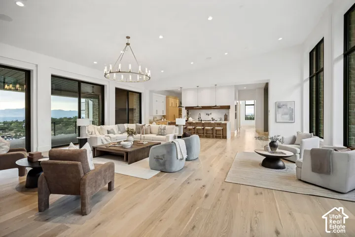 Open-concept living space featuring wood-finish flooring, a large circular chandelier, tall windows, and sliding glass doors to an outdoor area