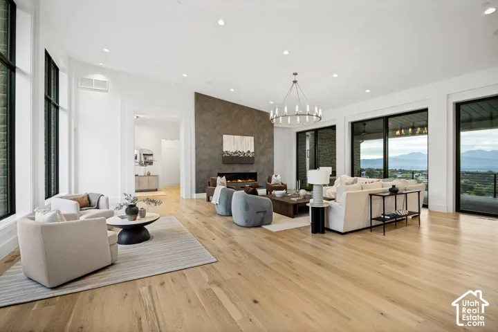 Spacious living area featuring light wood-finish flooring, a contemporary chandelier, a fireplace with a textured surround, large sliding glass doors, and expansive windows