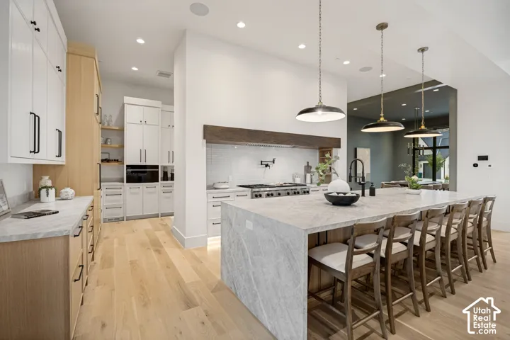 Gourmet kitchen featuring a large waterfall-edge island, integrated appliances, natural wood-finish flooring, and pendant lighting