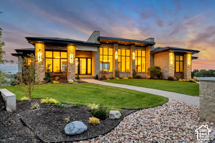 Stone veneer exterior with prominent columns, expansive windows, a paved walkway, and manicured landscaping featuring decorative rock beds