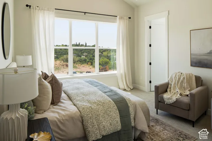 Bright bedroom with a large multi-pane window, light-toned carpeting, and a white interior door with dark hardware