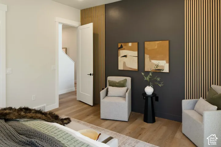 Wood-finish flooring, accent wall with vertical wood paneling, dark accent wall, white interior door with black hardware, and light-toned walls