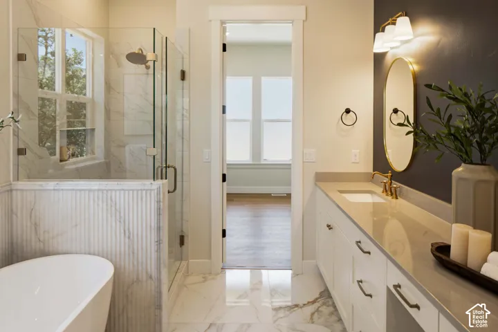 Freestanding soaking tub, glass-enclosed shower, marble-finish tile flooring, dual-sink vanity with light-colored countertop, and a contemporary wall-mounted light fixture