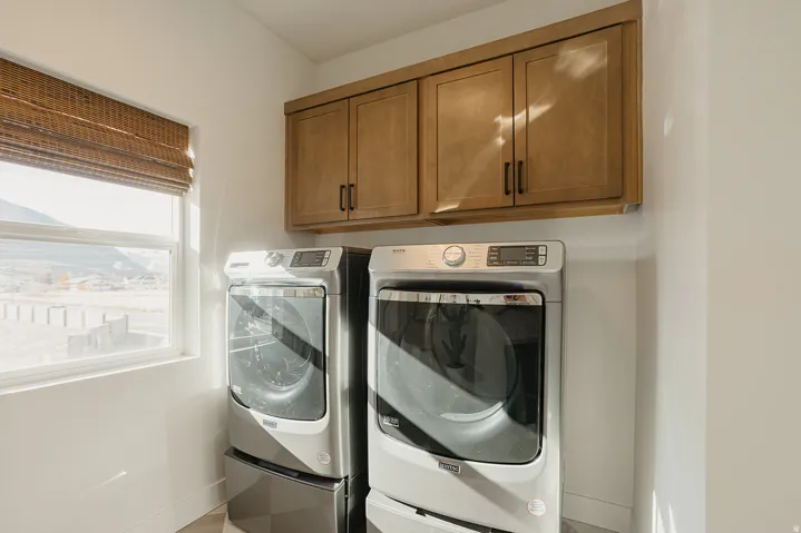 Laundry area featuring upper cabinetry, a single window, and a woven wood-finish blind