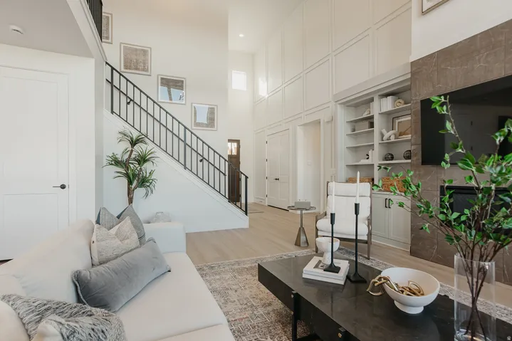 Two-story ceiling, wood-finish flooring, built-in shelving, fireplace with stone surround, and paneling accent walls