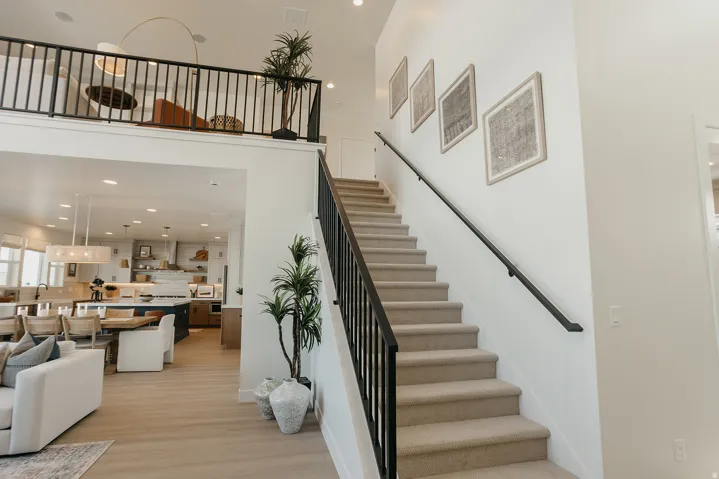 High ceilings with an open loft area, a carpeted staircase with a black metal railing, and wood-finish flooring