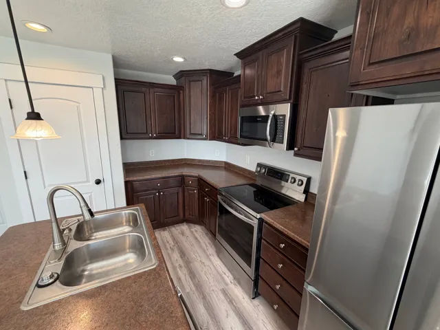 Kitchen featuring wood-finish flooring, dark wood cabinetry, stainless steel appliances, and a double basin sink with a pull-down faucet