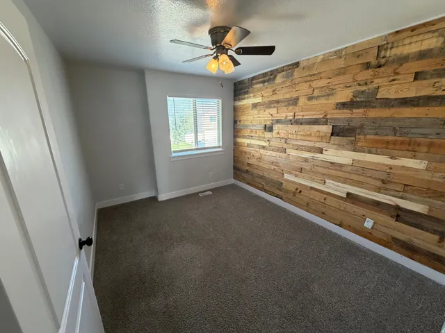 Textured accent wall, neutral carpet flooring, recessed window, and ceiling fan with integrated lighting