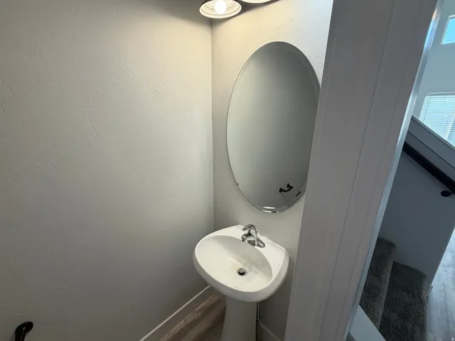 Pedestal sink with chrome faucet, oval wall-mounted mirror, and overhead vanity lighting
