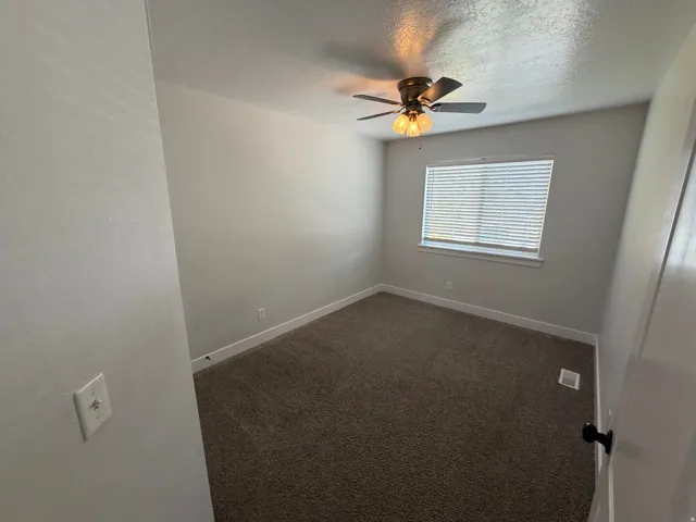 Neutral wall finishes, textured carpeting, window with blinds, and a ceiling fan with integrated lighting