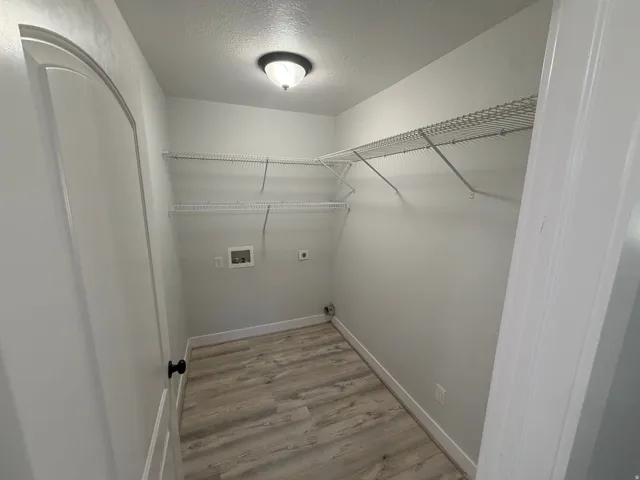 Laundry area with wood-finish flooring, overhead lighting, and wire shelving