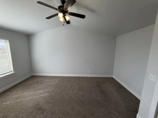 Vaulted ceiling, ceiling fan with integrated lighting, window with blinds, light gray walls, and brown carpeting
