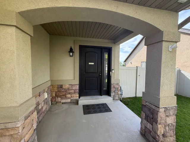 Covered entry with stucco and stone veneer accents, an arched ceiling, and an exterior sconce light