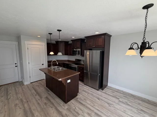 Kitchen featuring wood-finish flooring, dark wood cabinetry, a center island with sink, and stainless steel appliances