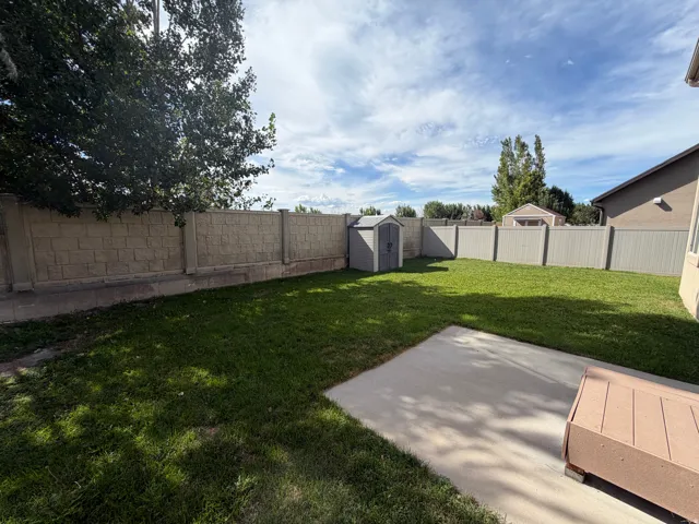 Expansive lawn featuring a concrete patio, a storage shed, and a block wall privacy fence