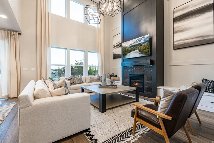 Two-story living area with high ceilings, large windows, a fireplace with a textured tile surround, and wood-finish flooring