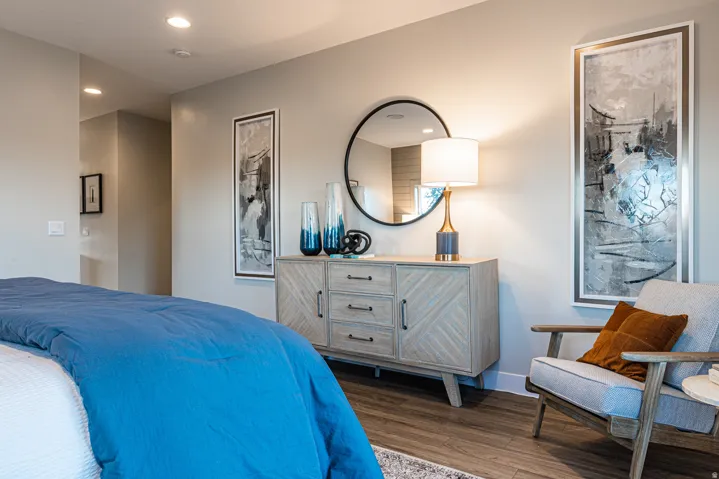 Recessed ceiling lighting, wood-finish flooring, light gray wall paint, and a wood-tone dresser with dark hardware