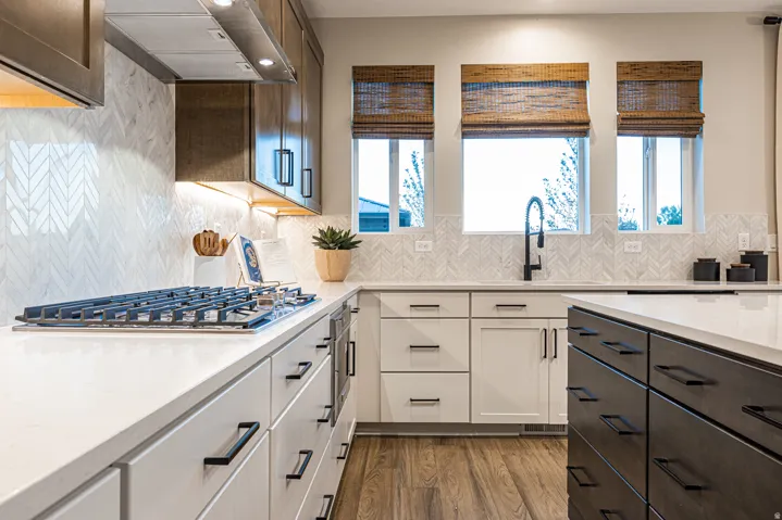 Chef's kitchen featuring white cabinetry with brushed metal hardware, white subway tile backsplash in herringbone pattern, quartz countertops, professional-grade gas cooktop, undermount sink with matte black faucet, and wood-finish flooring throughout