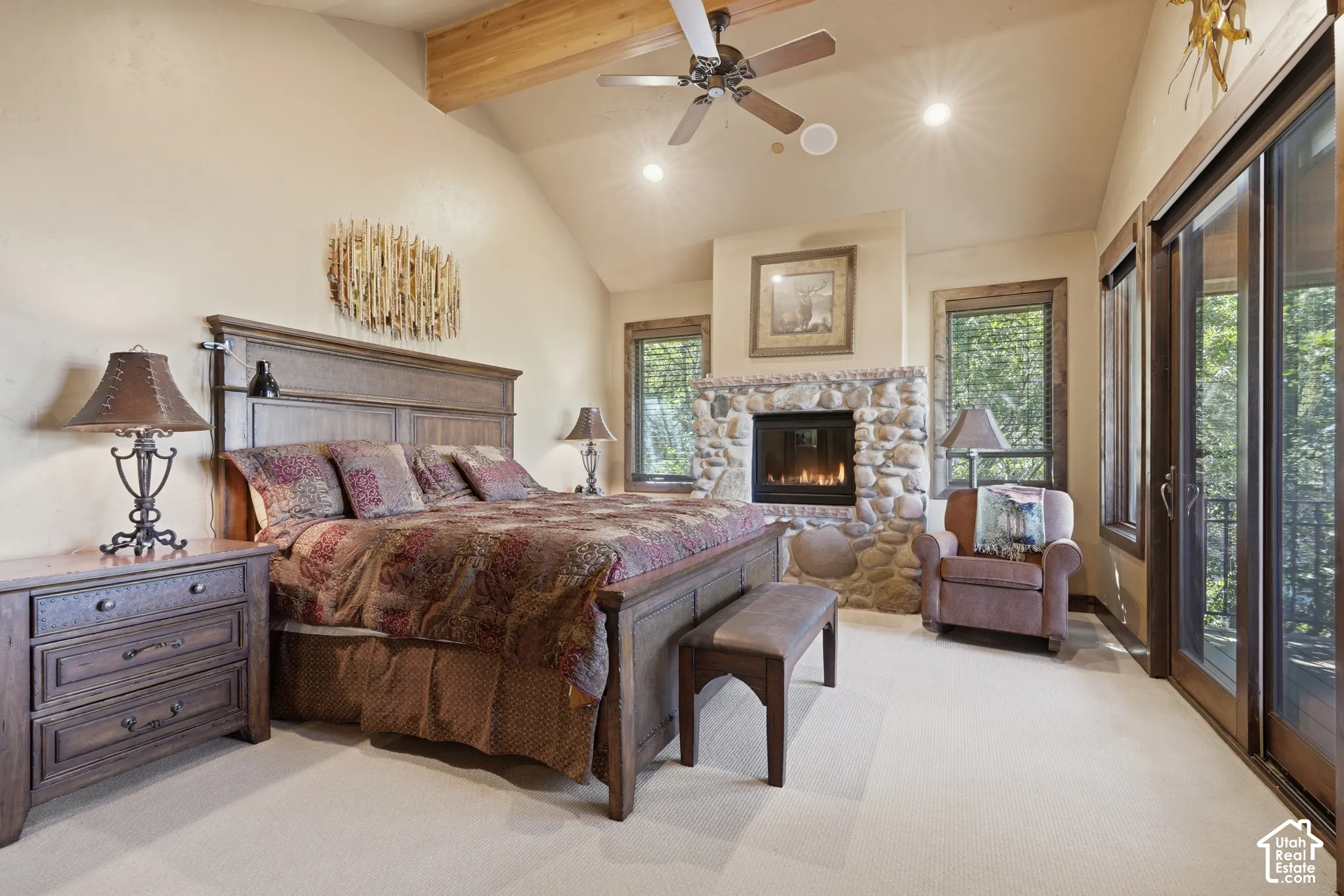Vaulted ceiling with exposed wood beams, stone-clad fireplace, recessed lighting, ceiling fan, and sliding glass doors
